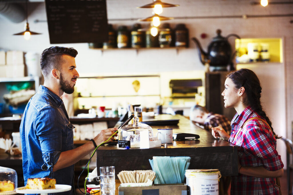 Specialist coffee shop. A man behind the counter using a touch screen to record transactions, and a woman customer.